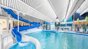 An indoor swimming pool with a blue slide, a lifeguard tower, and a restaurant in the background. - Luxury Chalet Near Beach (Kamperland)