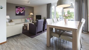 A modern living room with a dining area, a sofa, a TV, and a large window with curtains. - High-end Villa Nestled in Greenery (Arcen)
