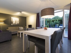 Relax in this stylish living area with a dining table for four, a comfortable sofa, and a large window offering a view of the outdoors.