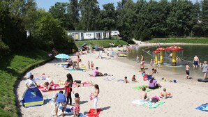 A beach with people sunbathing and swimming, a water play area, and a row of beach umbrellas. - High-end Villa Nestled in Greenery (Arcen)