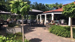 An outdoor patio area with tables and chairs, surrounded by greenery and a covered seating area. - Villa in Arcen With Shower and Sauna (Arcen)