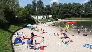 A beach with people sunbathing, swimming, and playing. There are tents, umbrellas, and a water slide. - Villa in Arcen With Shower and Sauna (Arcen)
