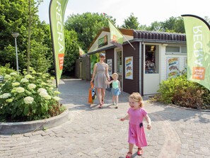 A paved pathway leading to a small building with flags and signs advertising local food and beverages. - Villa in Arcen With Shower and Sauna (Arcen)