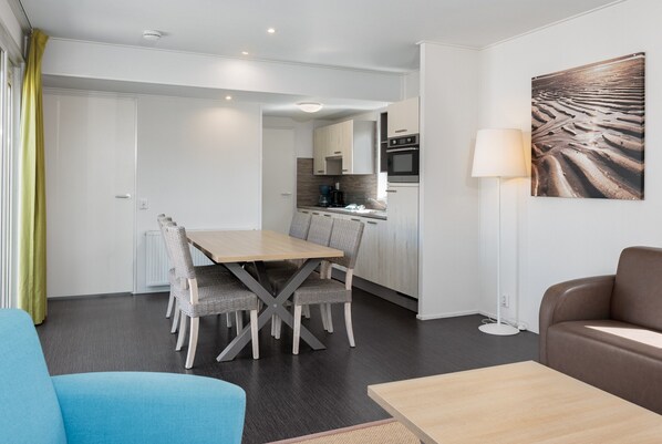 Un salon moderne avec un coin repas, une cuisine à l’arrière-plan et une grande fenêtre avec des rideaux.