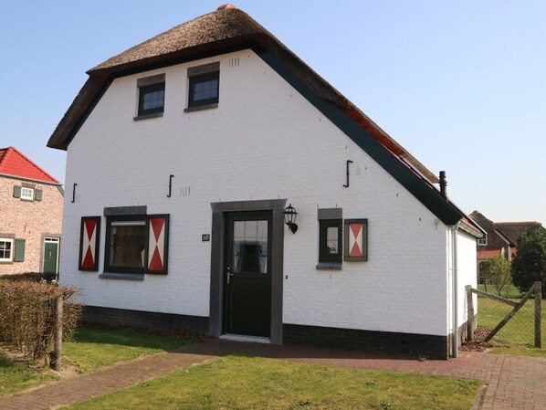 Een wit gebouw met een zwarte deur, ramen en een rieten dak.