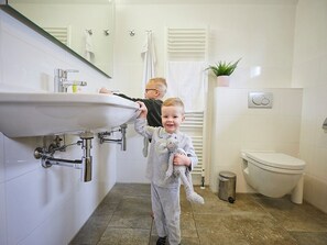 Een badkamer met een wastafel, spiegel, handdoekhouder, toilet en een kleine plant in pot.