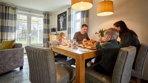 A dining area with a wooden table, grey upholstered chairs, and pendant lights. - Villa With Garden in Holiday Park in Limburg (Roggel)