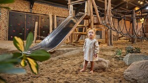 A child standing in a sandy play area with a slide and climbing structures. - Villa With Garden in Holiday Park in Limburg (Roggel)
