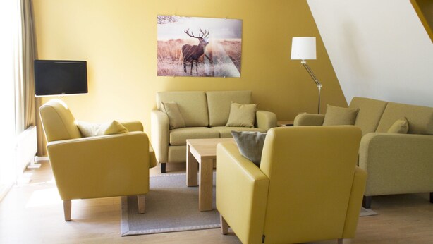 A modern living room with a sofa, armchairs, a coffee table, a flat-screen TV, and a painting of a deer. - Forest-edge Family Bungalow (Hoenderloo)