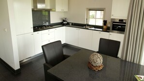 A modern kitchen with white cabinets, a black countertop, and a dining area with two chairs. - Villa With Bubble Bath (Hellendoorn)
