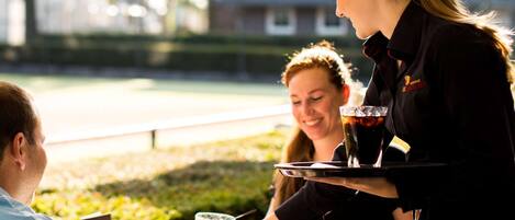 Una persona sirviendo bebidas en una mesa al aire libre, con una cerveza en un vaso y una botella de Amstel.