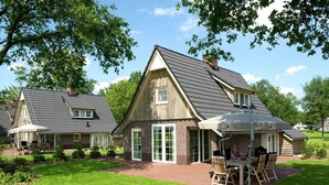 A two-story house with a sloped roof, a patio with outdoor furniture, and a well-maintained lawn. - Villa With Bubble Bath (Hellendoorn)
