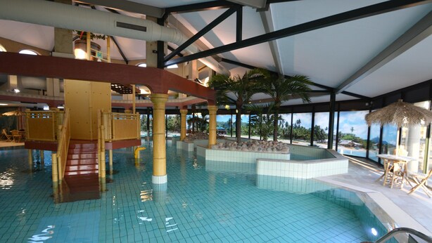 Una piscina interior con agua azul cristalina, una escalera central y vistas al exterior a través de amplios ventanales.
