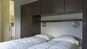A bedroom with two single beds, a dark wooden wardrobe, and a small round mirror on the wall.