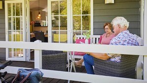 A covered outdoor seating area with wicker furniture and a table, overlooking a garden. - Cozy Lodge With a Dishwasher in the Achterhoek (Winterswijk - Brinkheurne)
