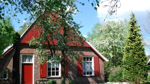 A brick house with red shutters and a white door, surrounded by greenery and trees. - Cozy Lodge With a Dishwasher in the Achterhoek (Winterswijk - Brinkheurne)