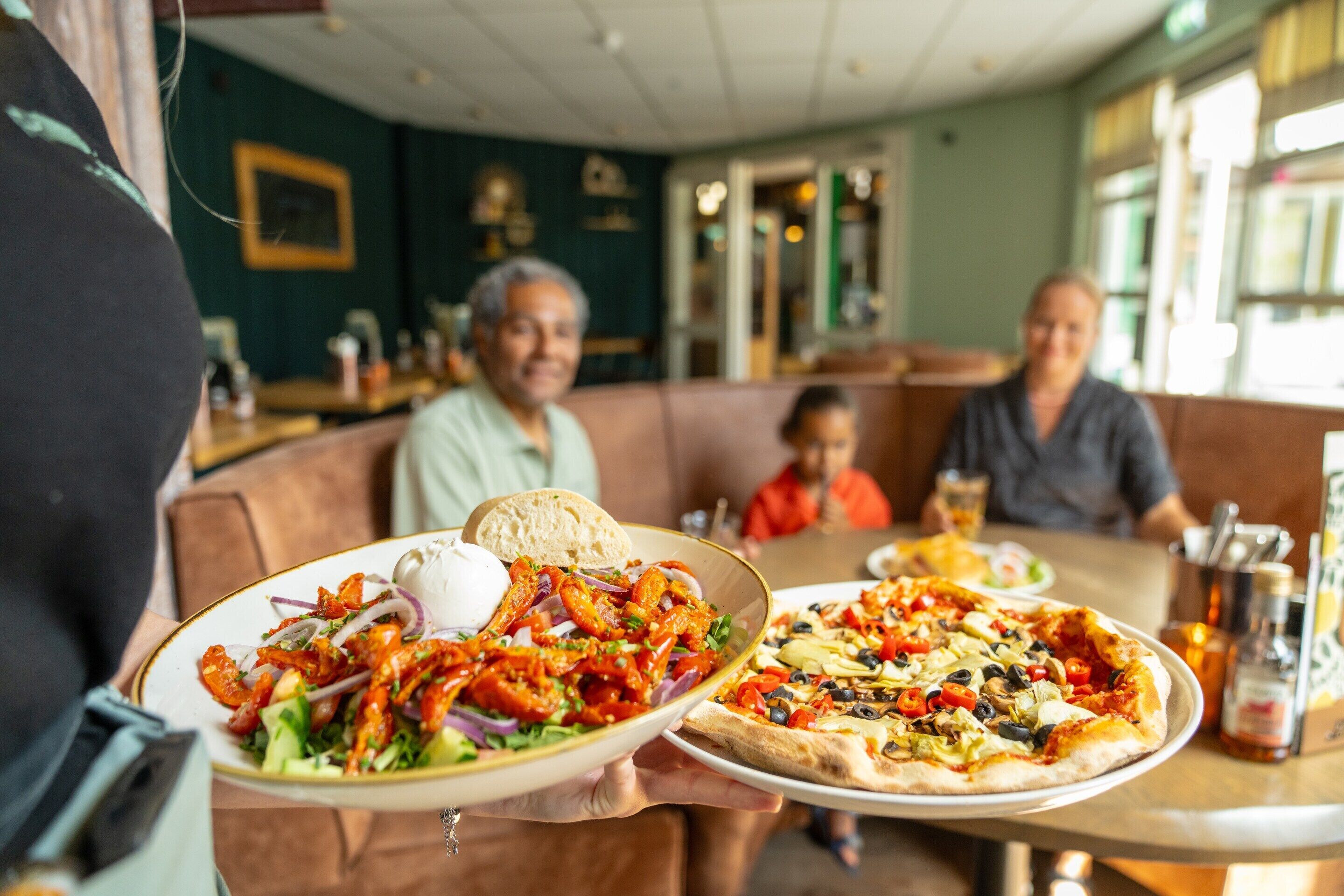 A restaurant with a booth seating area and a table with a pizza and salad.