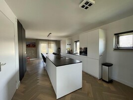 Una cocina moderna con una isla central, un comedor con sillas y una pequeña zona de bar.