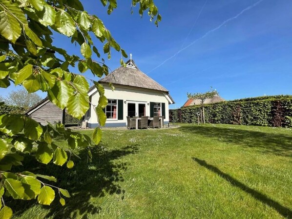 Une maison avec un toit de chaume, une pelouse et une haie.