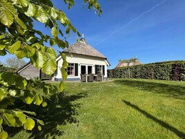 A house with a thatched roof, a lawn, and a hedge.