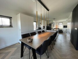 A modern kitchen with a long dining table, black chairs, and pendant lights.
