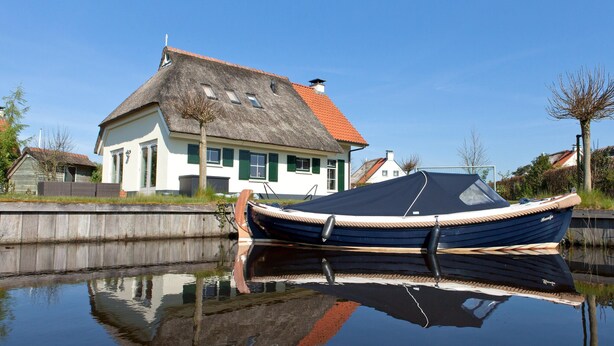 A house with a thatched roof and a boat docked in a calm water body. - Country House with Terrace near Langweerder Wielen (Sint Nicolaasga)