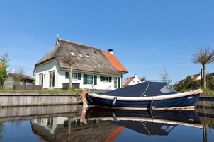 A house with a thatched roof and a boat docked in a calm water body.