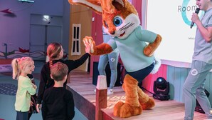A person in a rabbit costume on a stage with a microphone, a projection screen displaying "Room," and a child interacting with the character. - Forest Stay With Shared Pool (Borger)