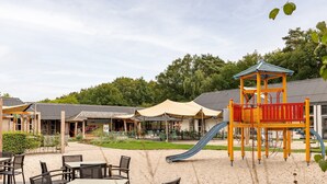 A playground with a slide and a climbing structure, surrounded by outdoor seating and covered areas. - Forest Stay With Shared Pool (Borger)