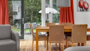 A dining area with wicker chairs, a wooden table, and a view of the outdoors through large windows. - Forest Stay With Shared Pool (Borger)