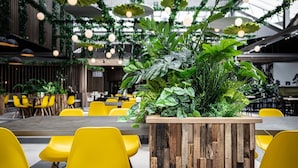 A modern indoor dining area with yellow chairs, a wooden planter with green plants, and hanging lights. - Nice Villa With a Sauna in Limburg (Roggel)