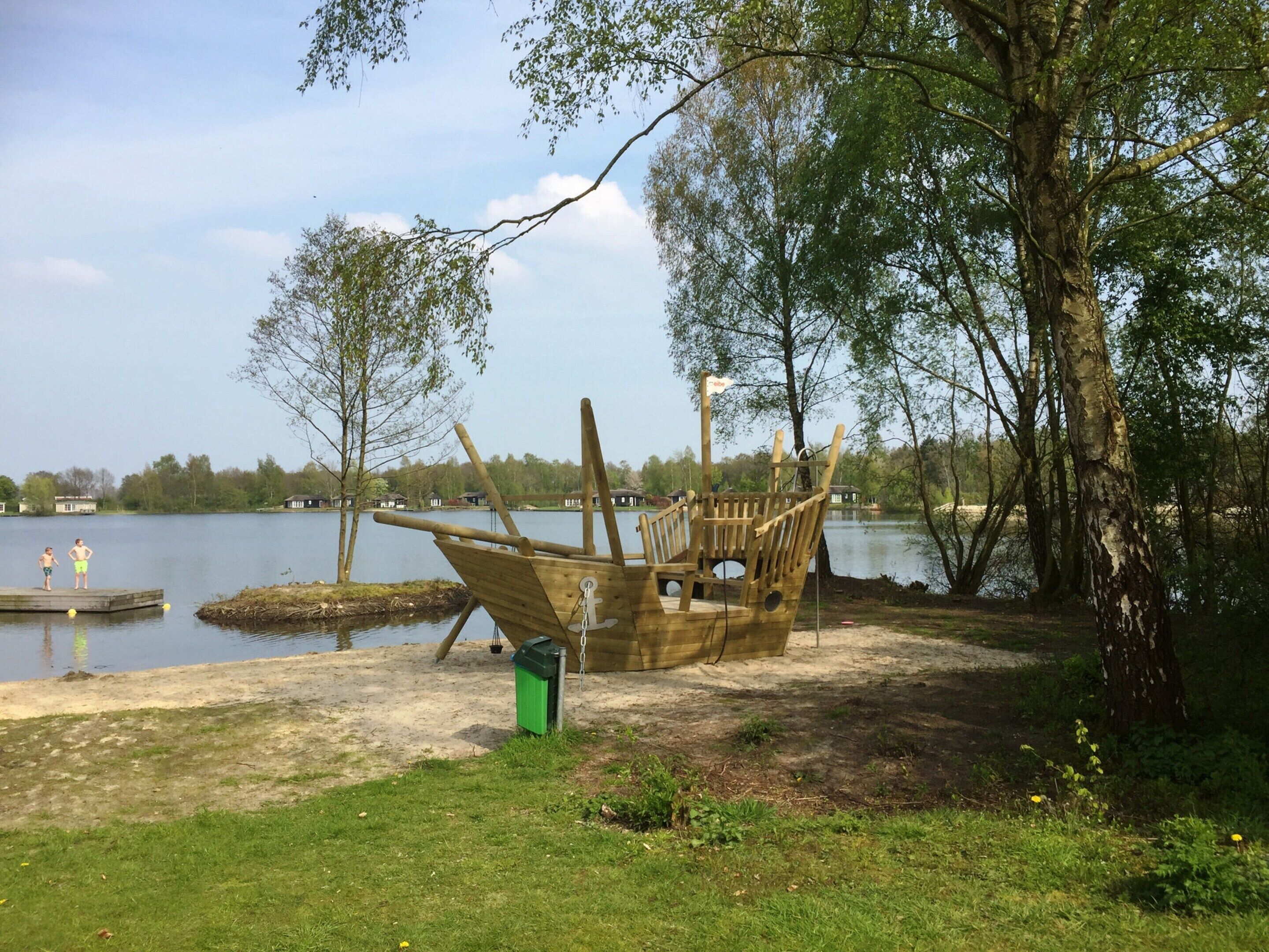 A wooden boat structure by a lakeside with a green trash bin nearby.