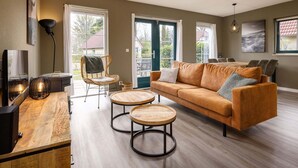 Ein geräumiges Wohnzimmer mit einer großen Couch, zwei runden Holztischen, einem Korbstuhl und einem Essbereich mit Stühlen.