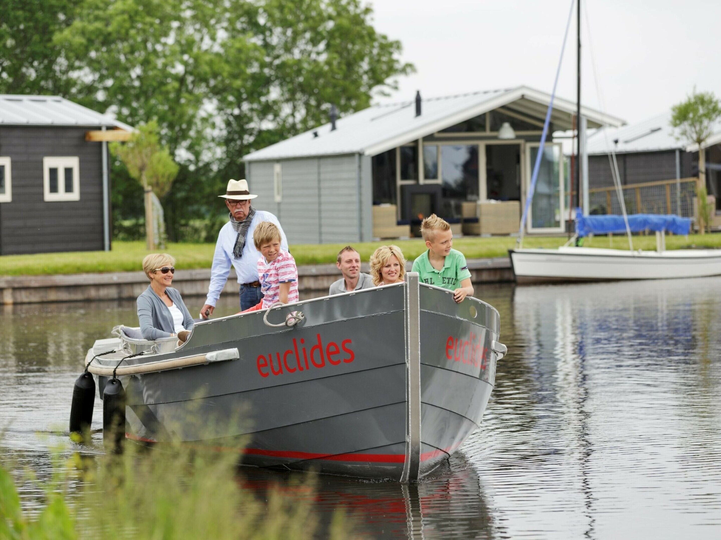 A boat with the name 'euclides' on its side, docked at a marina with houses in the background.
