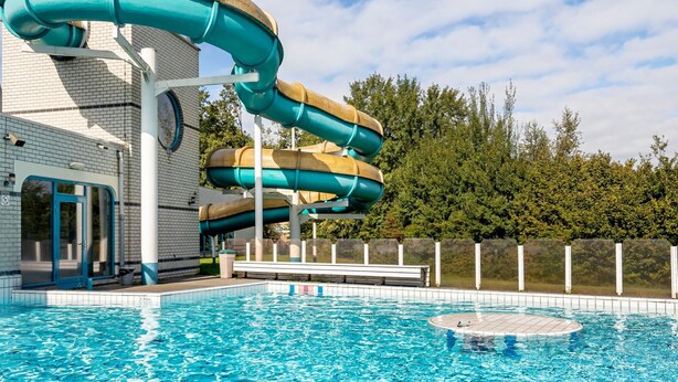 A water park with a multi-level water slide, a swimming pool, and a building with a brick facade. - Forest Trails & Swimming Fun (Borger)