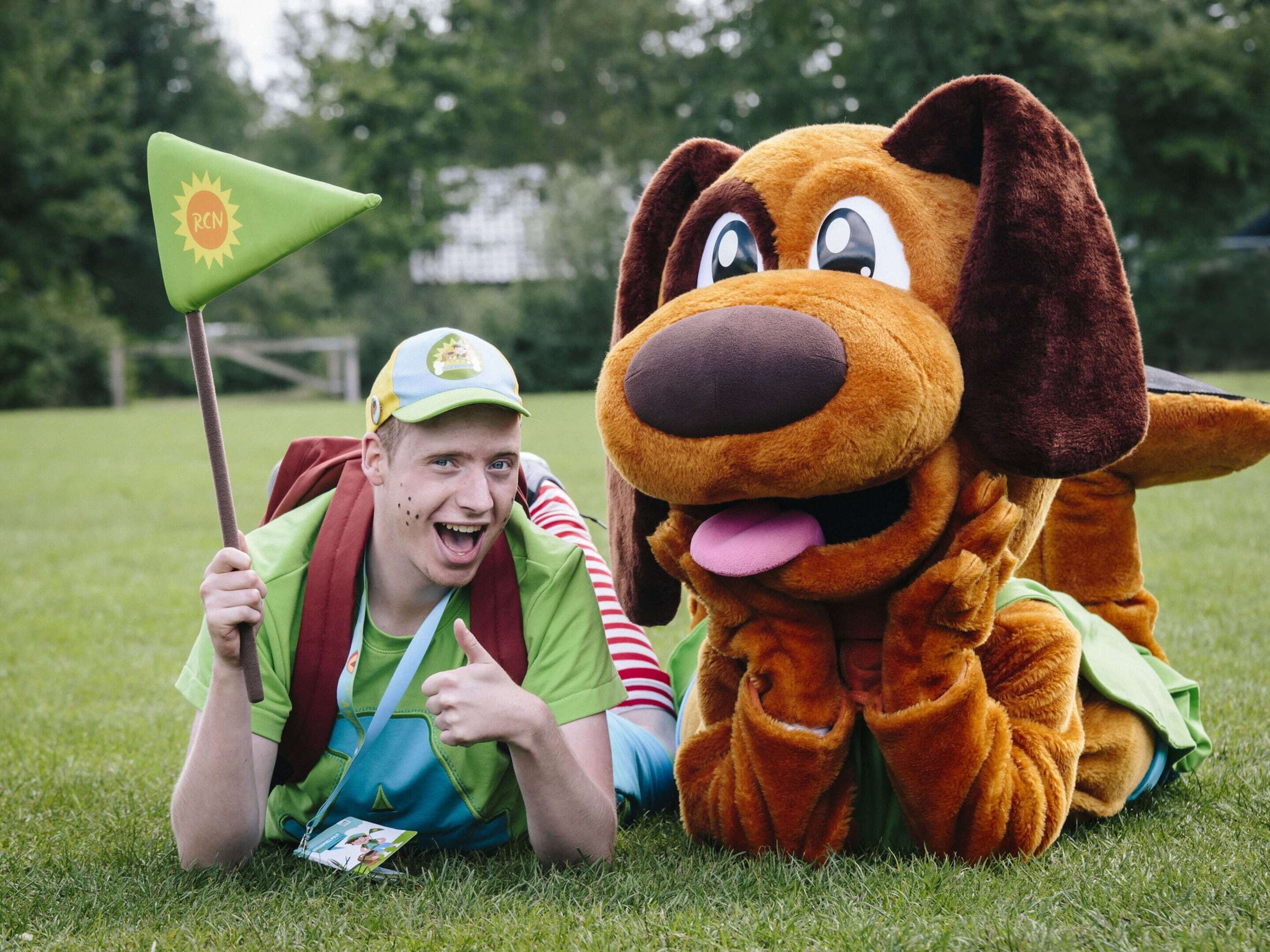 A person lying on grass with a large plush dog toy.
