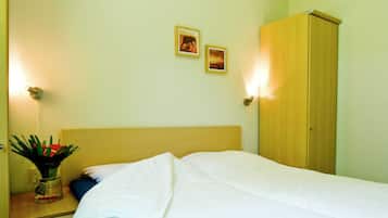 A hotel room with a bed, a nightstand with a vase of flowers, and two wall-mounted lamps.