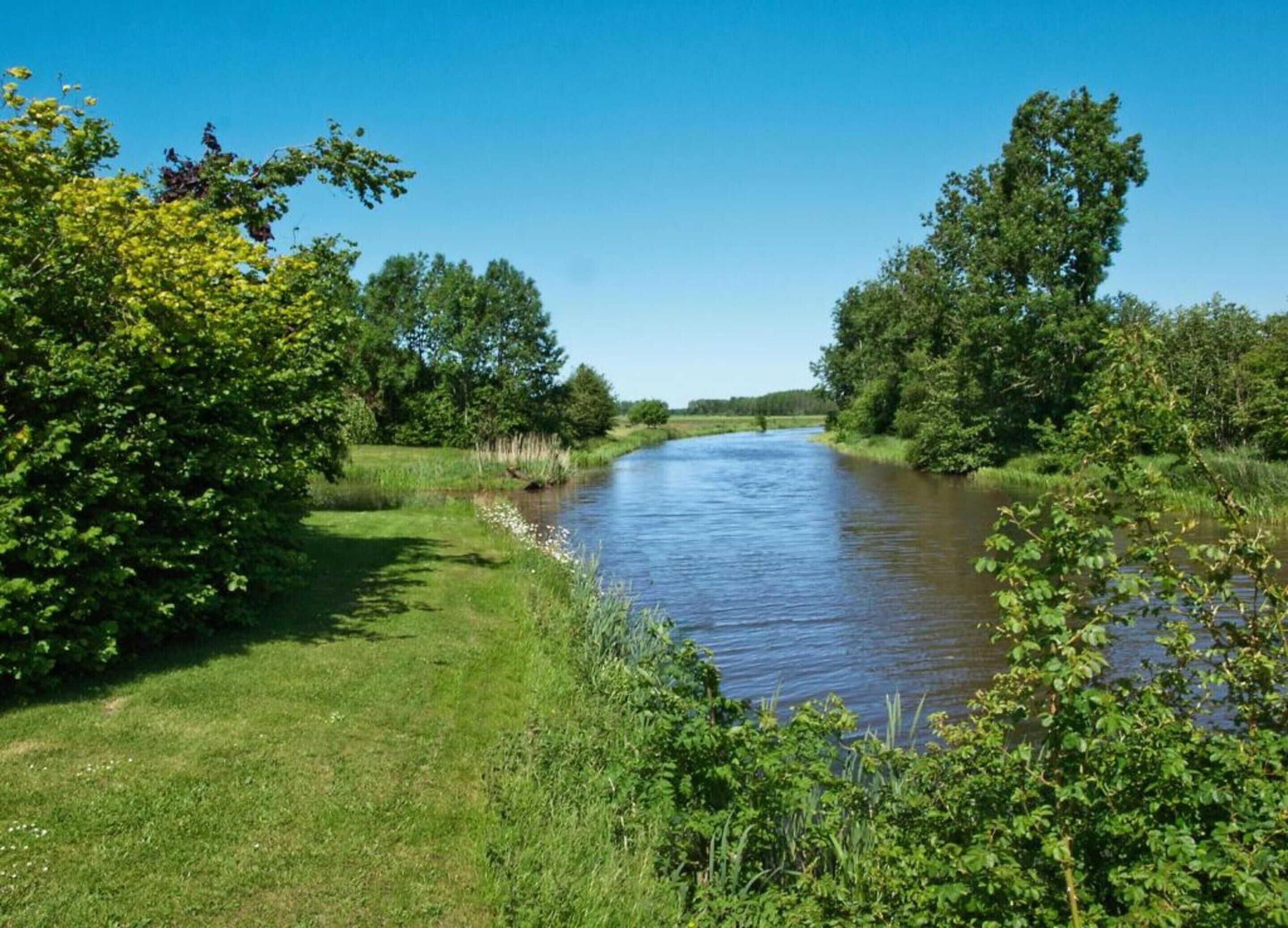 Een rivier omzoomd door weelderige begroeiing en bomen, met een helderblauwe lucht erboven.