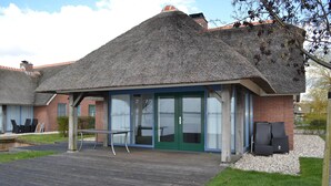 A building with a thatched roof, large glass doors, and a wooden deck. - Stylish Thatched Villa with 2 Bathrooms near Giethoorn (Wanneperveen)