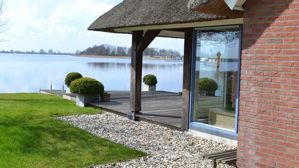 A building with a thatched roof, a glass door, and a view of a lake. - Stylish Thatched Villa with 2 Bathrooms near Giethoorn (Wanneperveen)