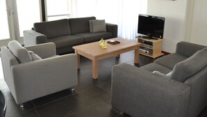 A modern living room with a grey sofa set, a wooden coffee table, and a flat-screen TV on a wooden stand. - Stylish Thatched Villa with 2 Bathrooms near Giethoorn (Wanneperveen)