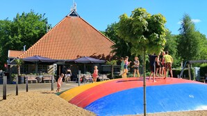 A beach with a colorful slide and a building with a tiled roof in the background. - Holiday House in Friesland With Garden (Sint Nicolaasga)