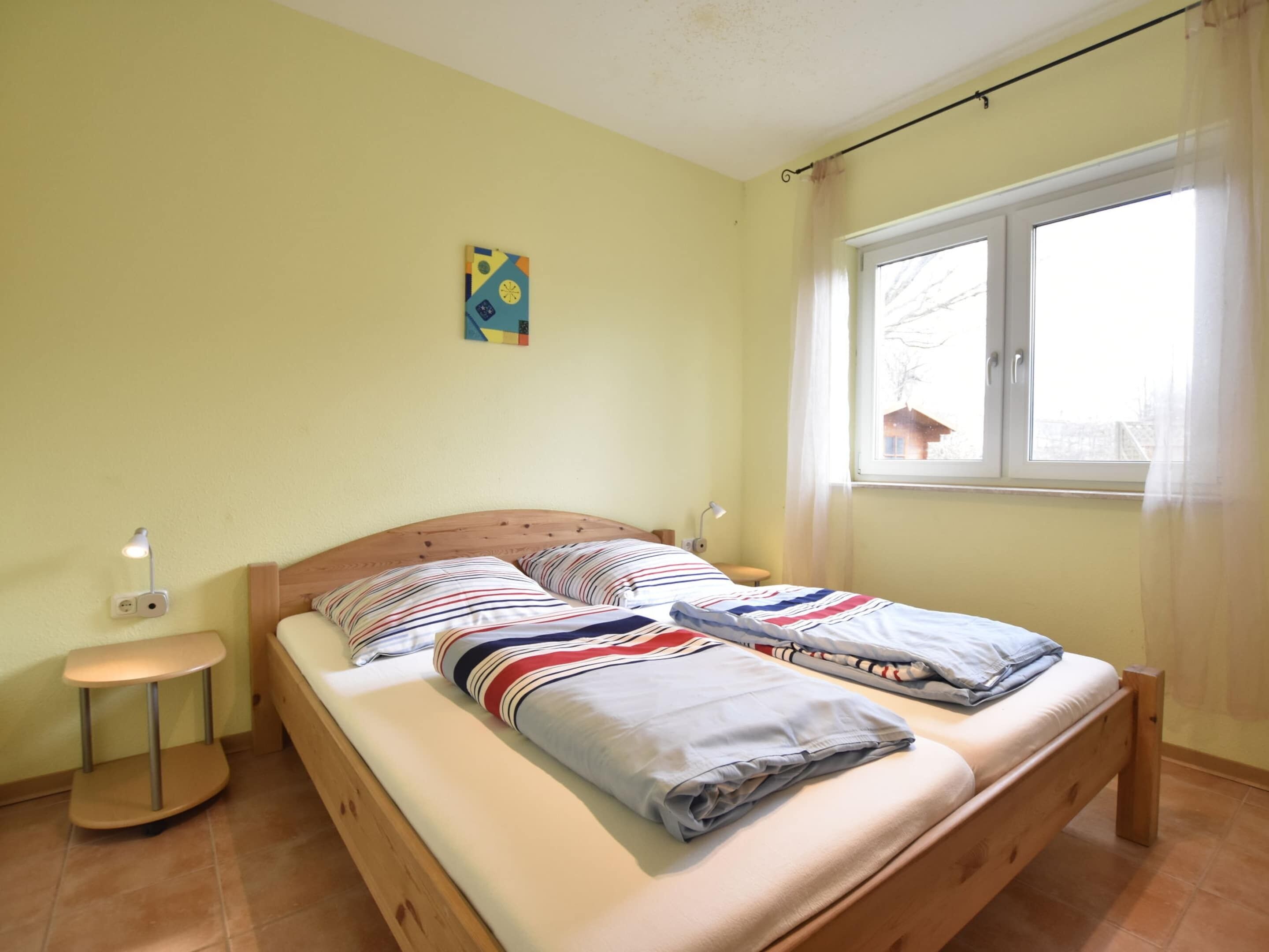 A single bed with striped bedding, a small bedside table, a lamp, and a window with curtains.