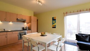 A modern kitchen with white cabinets, a dining table with chairs, and a black leather sofa.