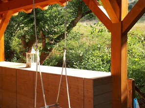 Una hamaca de madera con cuerdas, un farol y vista a la vegetación.