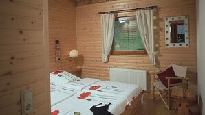 A wooden cabin bedroom with a bed, a chair, a window with curtains, a radiator, and a mirror on the wall. - Feriendorf Reinskopf in der Eifel (Schoenecken)