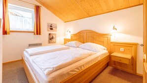 A bedroom with a wooden ceiling, a bed with white bedding, a nightstand, a wall-mounted lamp, and a window with curtains.