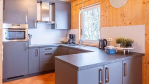 A modern kitchen with grey cabinets, stainless steel appliances, a built-in oven, and a window with a view of trees.