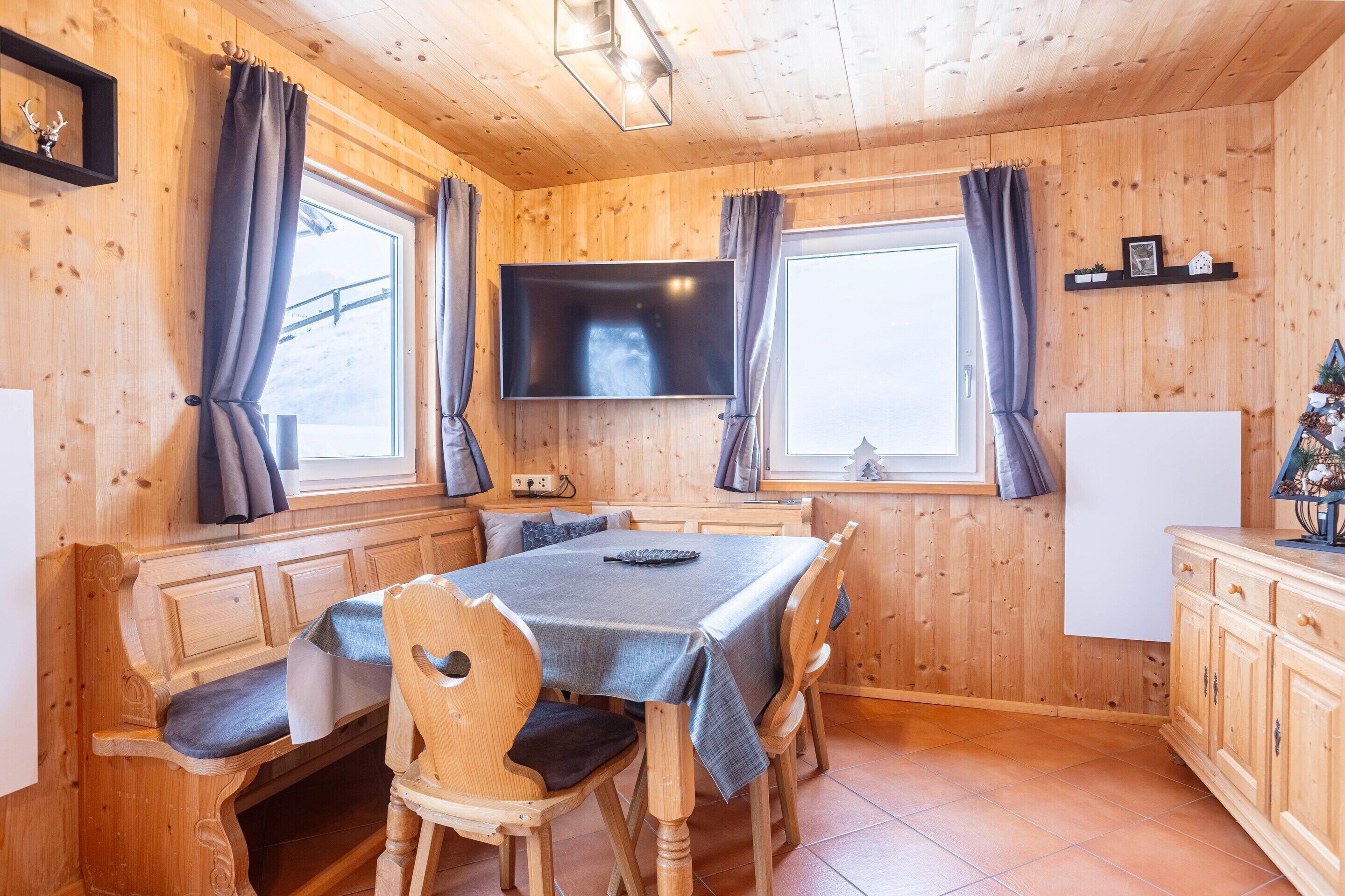 A wooden interior with a dining table, chairs, a TV, and a small Christmas tree.