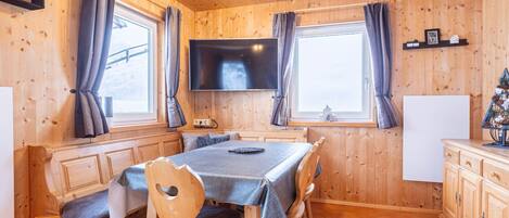 A wooden interior with a dining table, chairs, a TV, and a small Christmas tree.